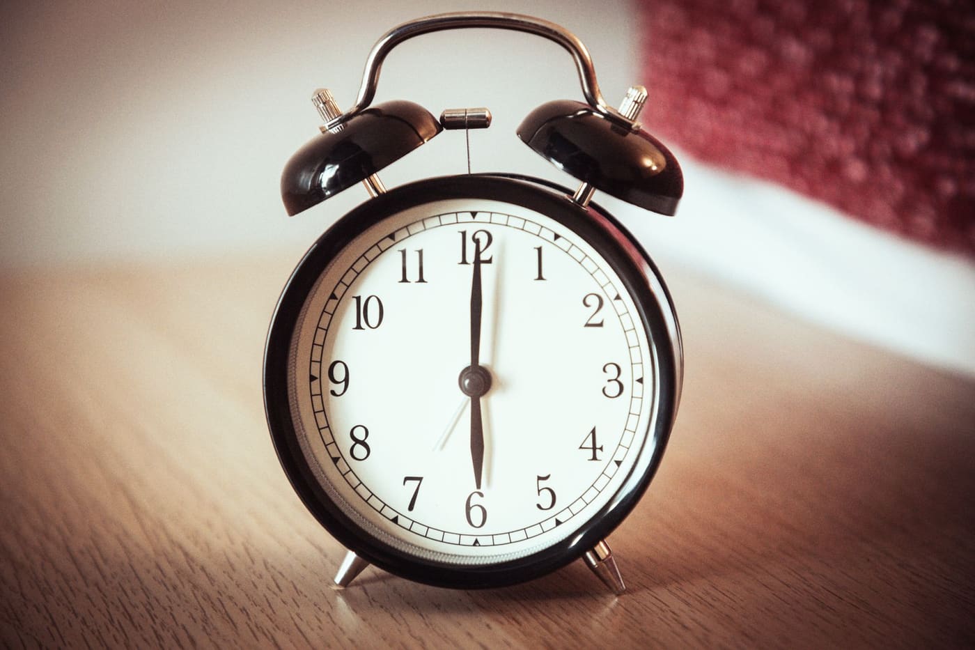 A black twin-bell alarm clock on a wooden table showing six o'clock