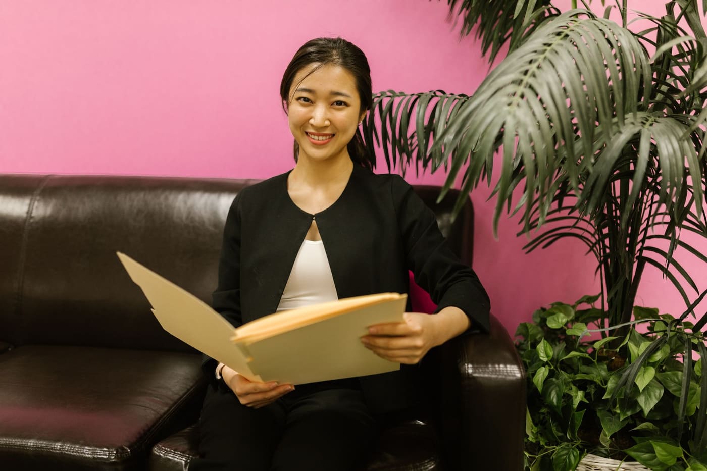 A smiling woman in business clothes sitting on a couch holding an open folder