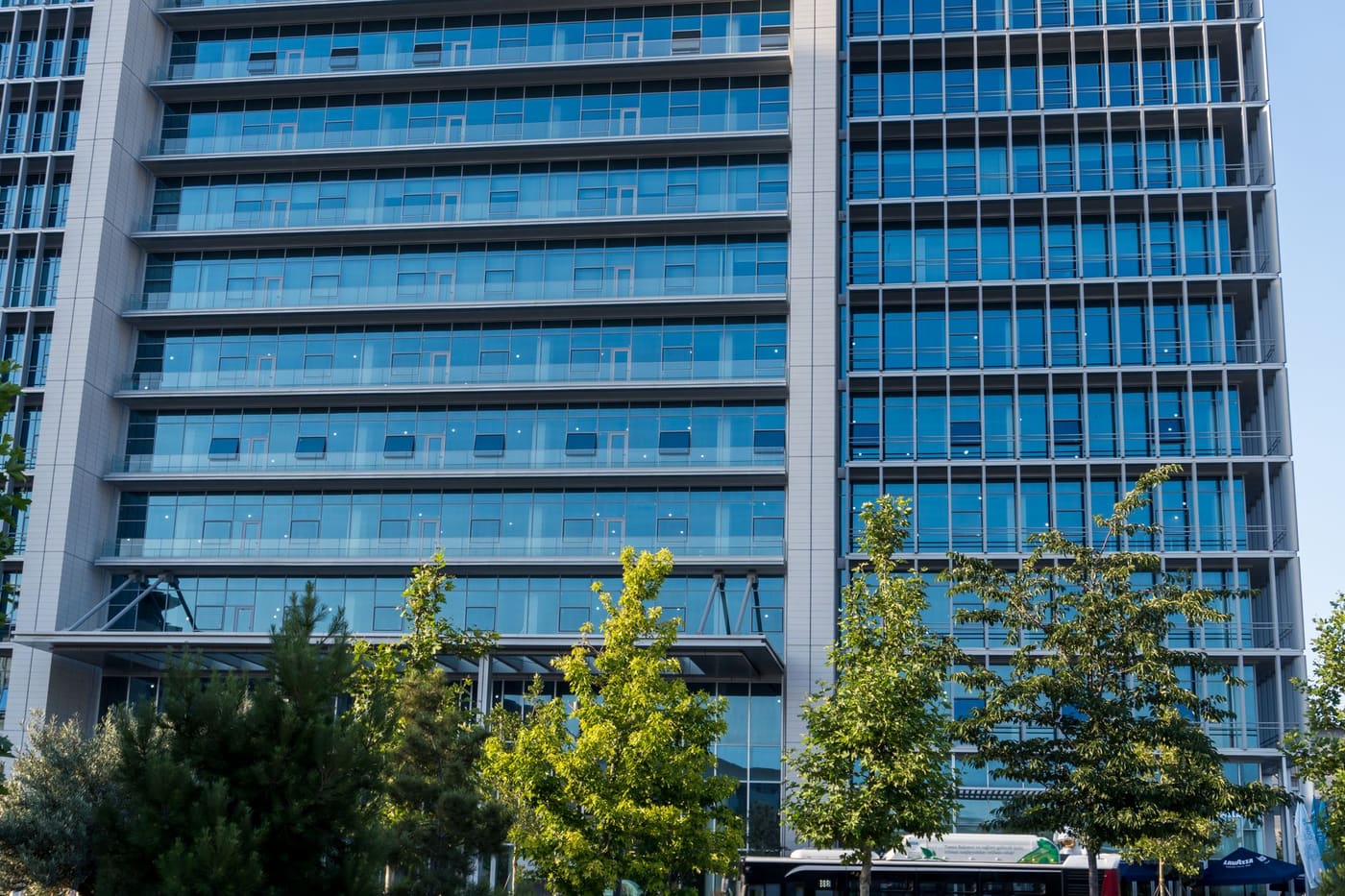 A glass-fronted office tower with trees in front of it on a sunny day