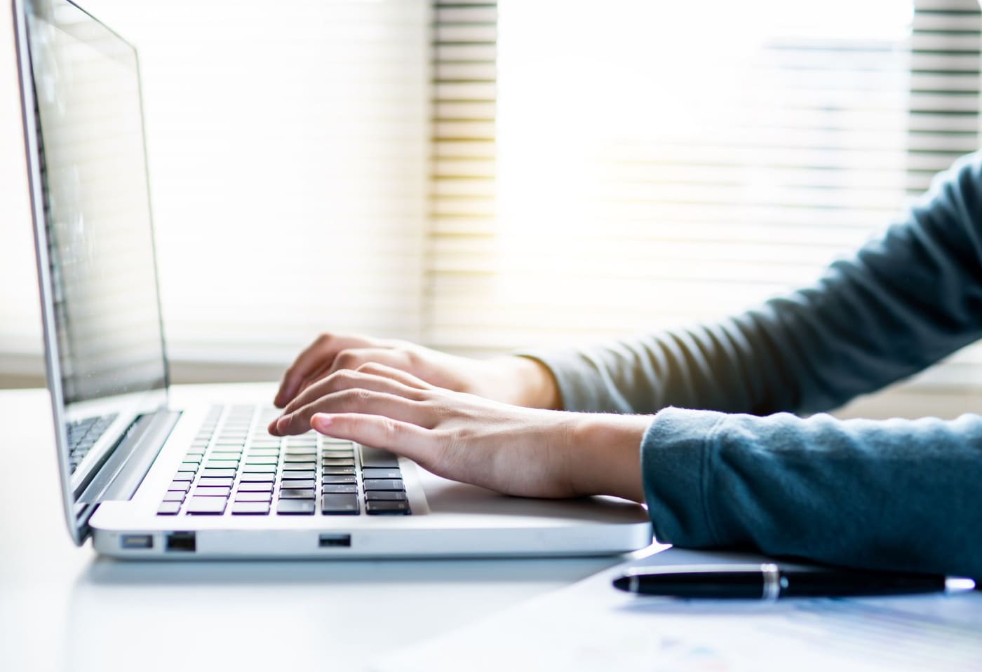 Hands typing on a laptop keyboard in a bright room