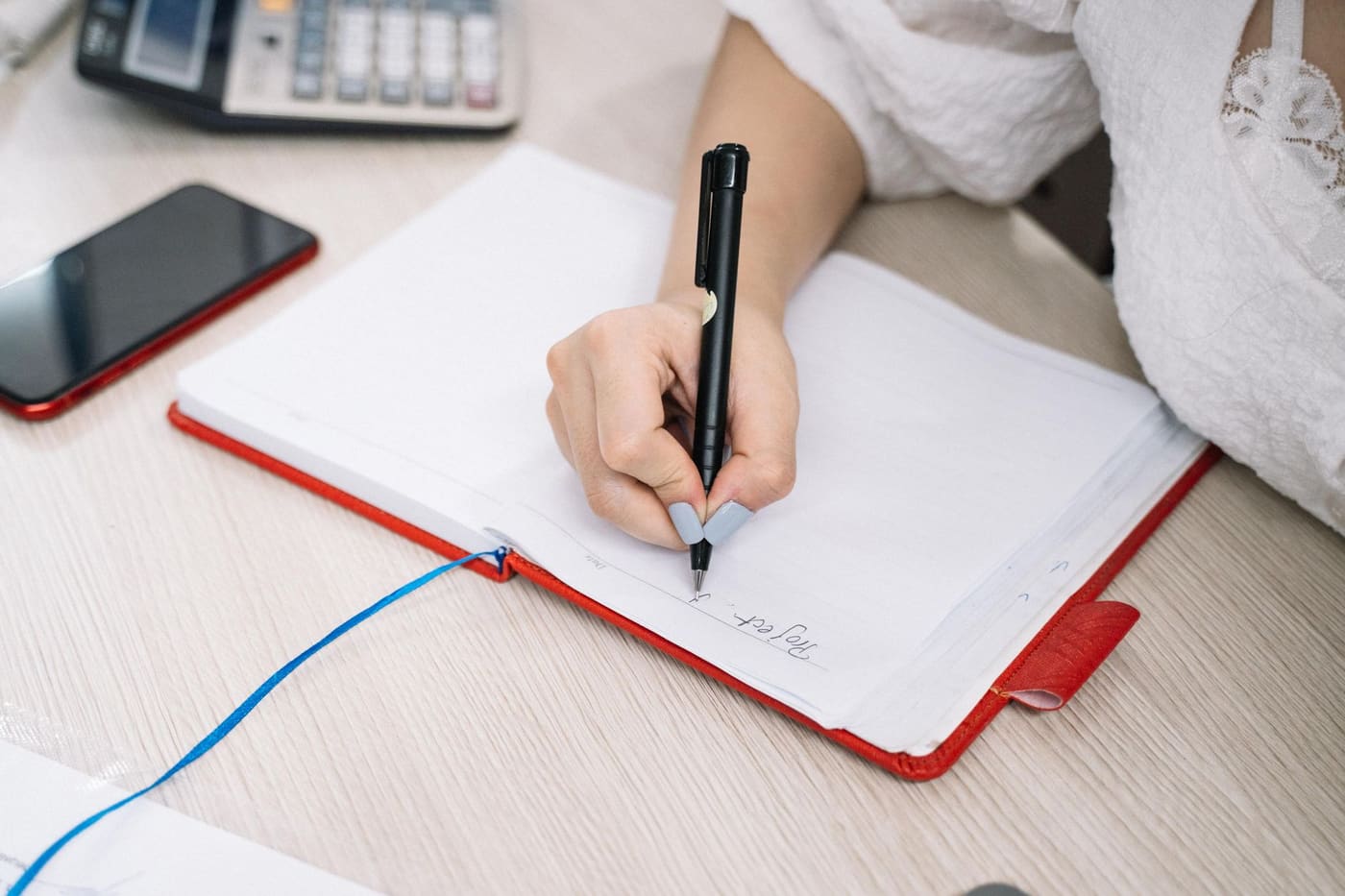 A hand writing bullet notes with a black pen in an open red notebook