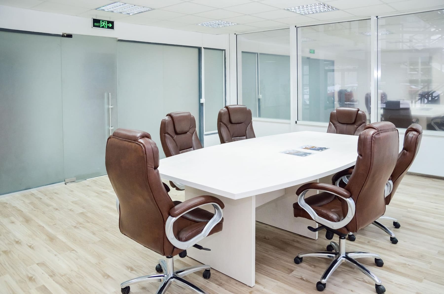 A bright, empty conference room with a white table and brown leather chairs