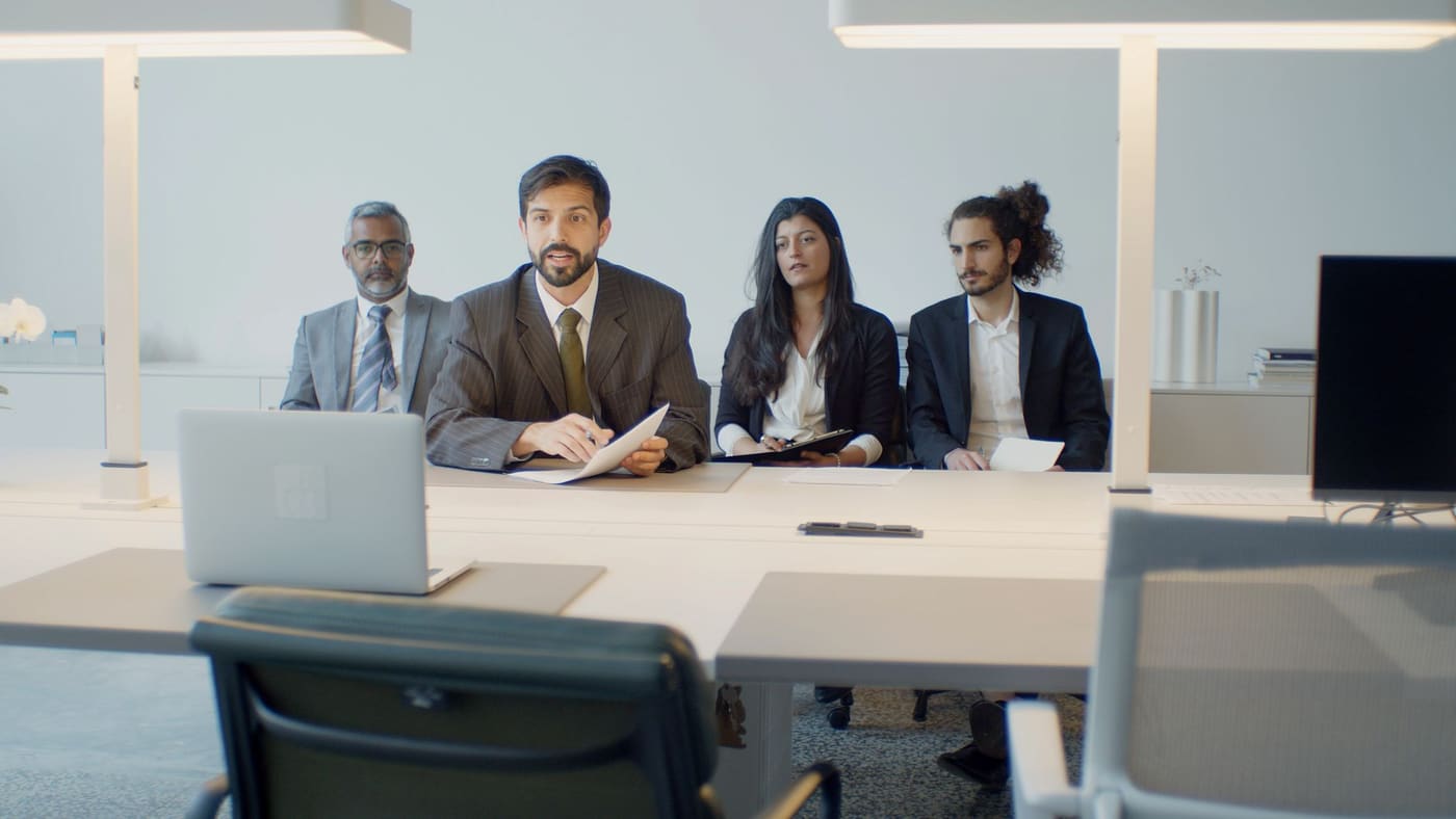 Four interviewers seated side by side at a long table in a bright office