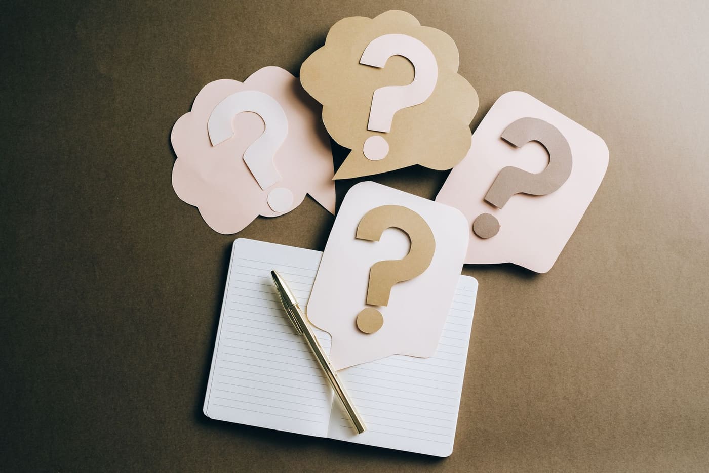 Paper question mark speech bubbles on a lined notebook with a pen